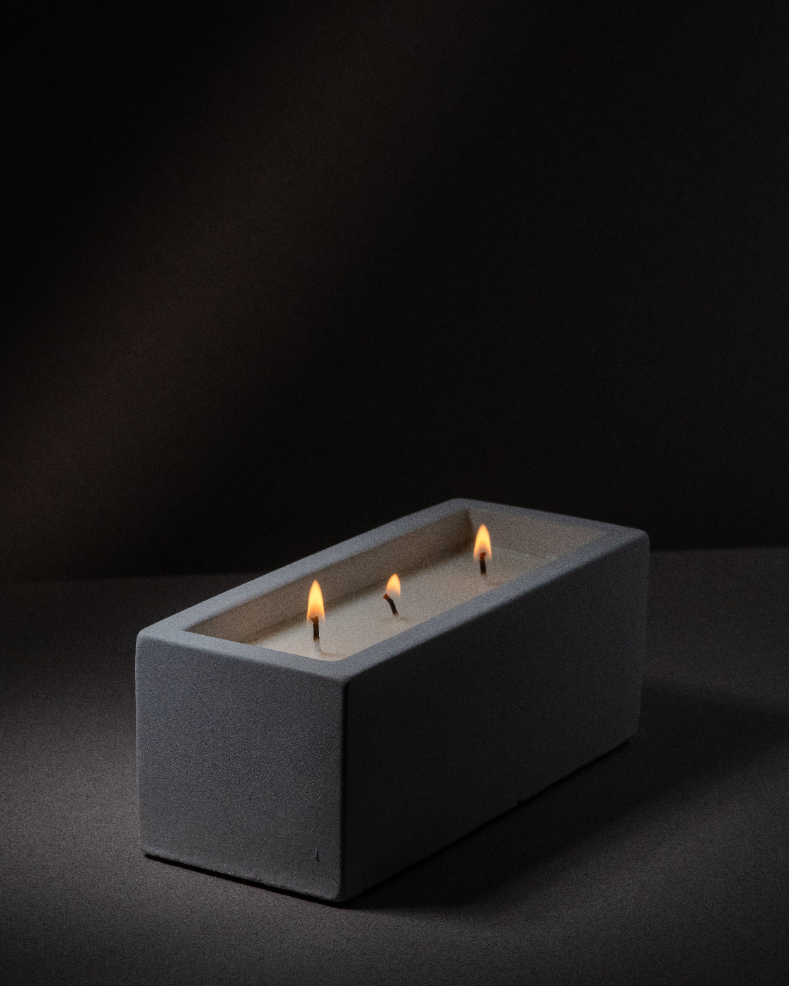 Rectangular concrete candle holder with three lit candles on a black background