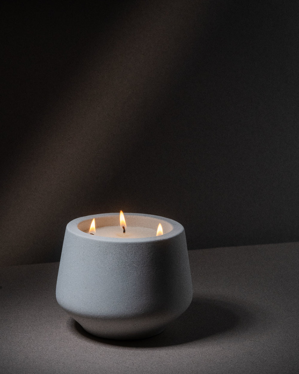 Ceramic candle holder with three lit candles on a dark background