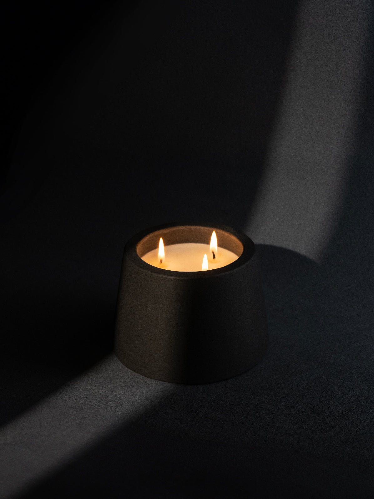 A black candle holder with a lit candle inside, casting a warm glow in a dark environment.